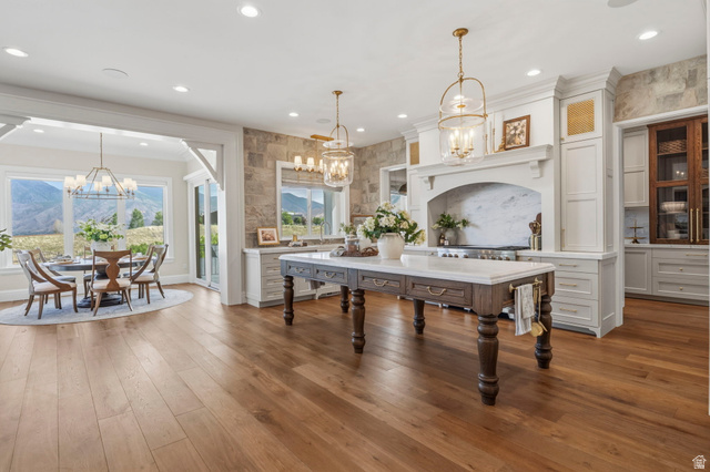 115 East Hidden Ridge Lane, Unit 42 Mapleton, UT 84664 - Photo 9 of 103 Open-concept kitchen and dining area featuring wood-finish flooring, a substantial kitchen island with a stone countertop, white cabinetry with gold-toned hardware, and a built-in range with a marble backsplash