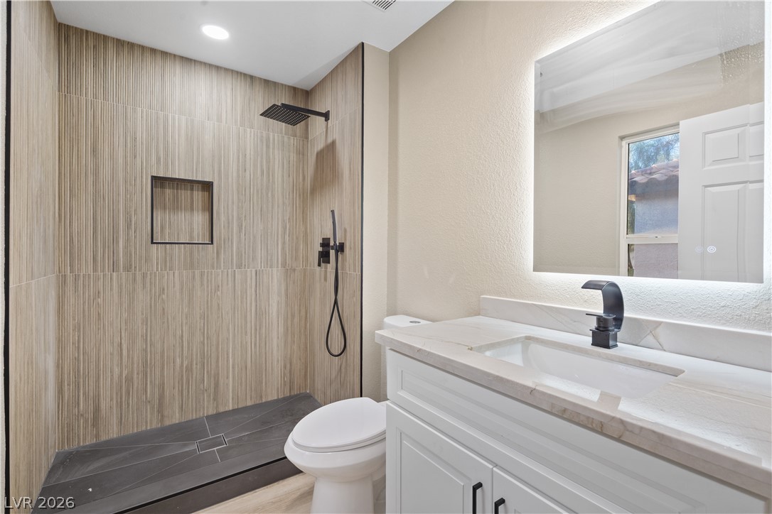 1662 Ravanusa Drive Henderson, NV 89052 - Photo 31 of 74 A well-lit, contemporary bathroom showcases a sleek vanity with an integrated sink and a modern, tiled walk-in shower.