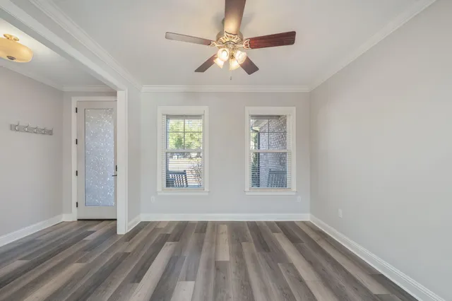 an empty room with wooden floor chandelier fan and windows