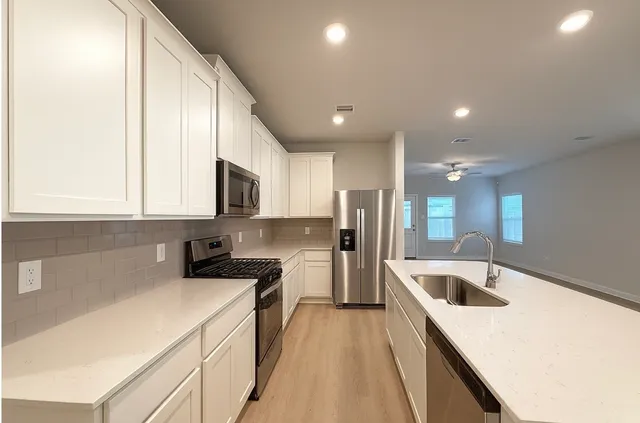 a kitchen with stainless steel appliances granite countertop a refrigerator oven a sink dishwasher and white cabinets with wooden floor