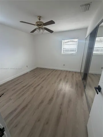 an empty room with wooden floor fan and windows