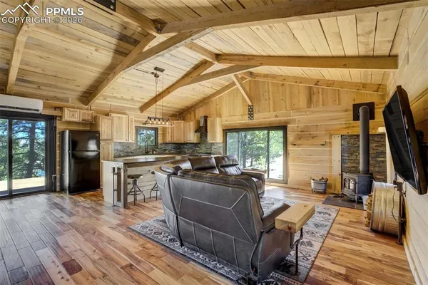 a living room with stainless steel appliances kitchen island granite countertop a sink and a wooden floors