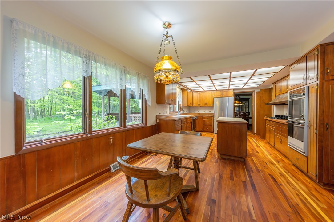 25001 Letchworth Road Beachwood, OH 44122 - Photo 14 of 50 Spacious kitchen featuring extensive wood-finish flooring, ample wood cabinetry, a central island, stainless steel appliances, and large windows overlooking a wooded exterior