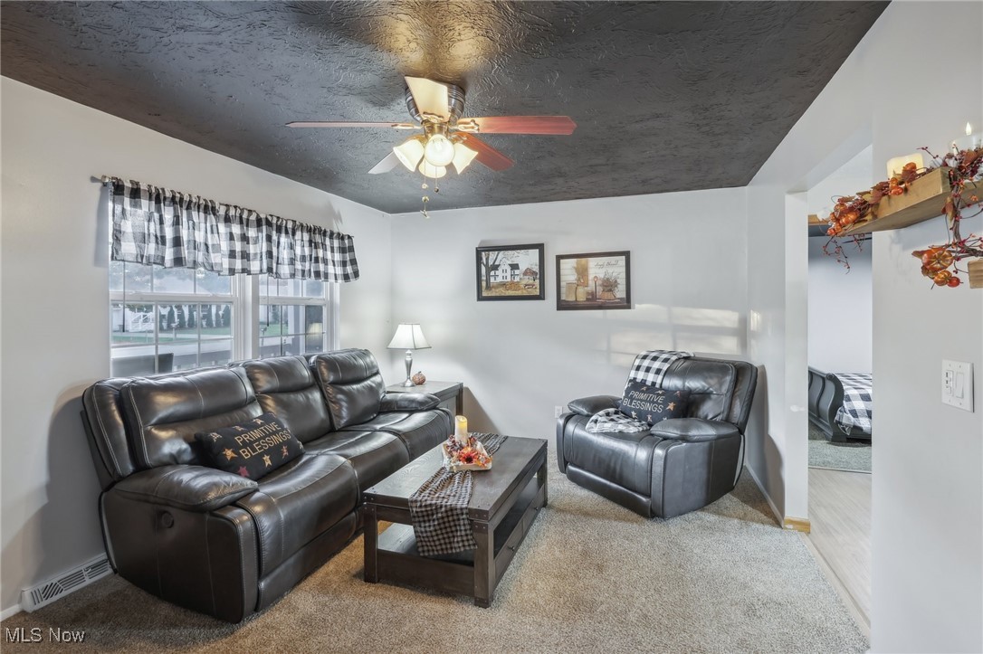 Living room featuring a textured ceiling, light colored carpet, and ceiling fan