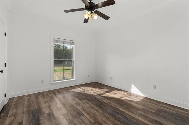 an empty room with wooden floor ceiling fan and windows