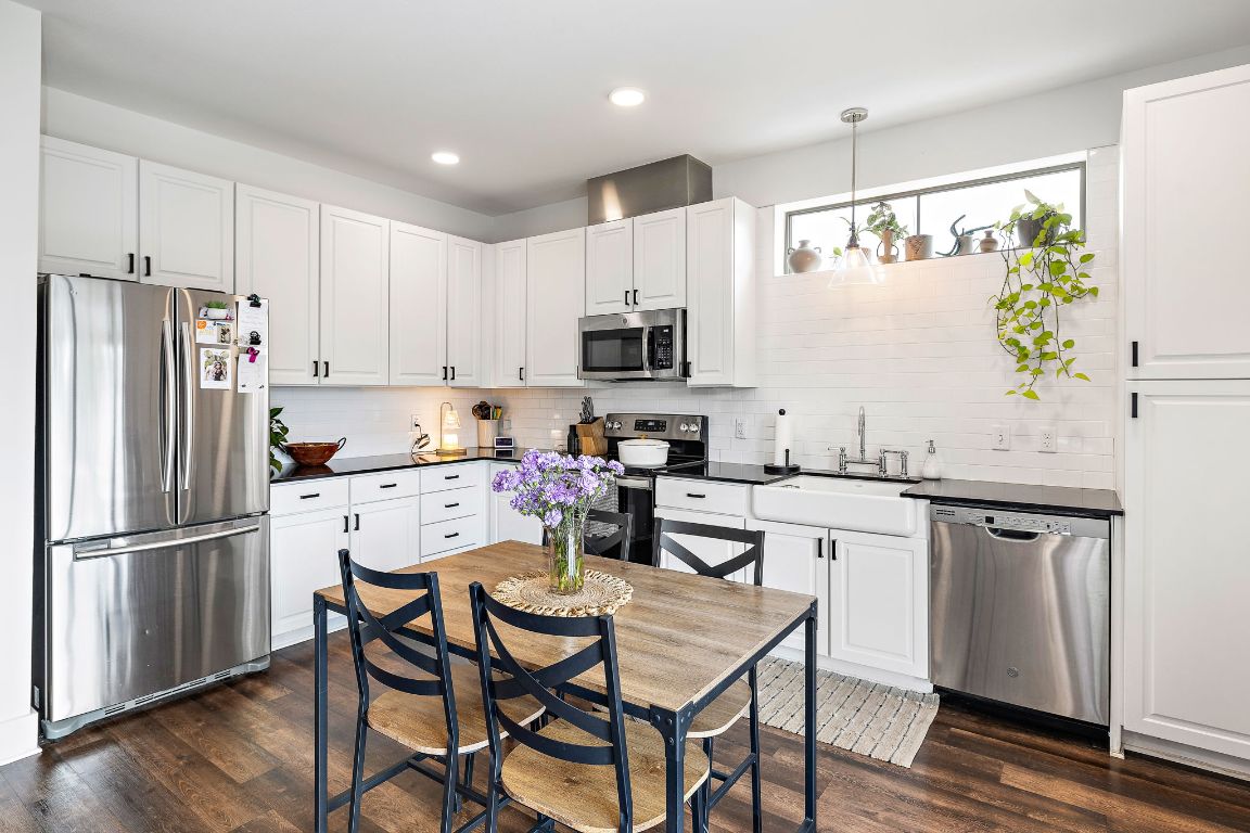 4704 Sunset Trail, Unit 1101 Austin, TX 78745 - Photo 8 of 23 Kitchen with appliances with stainless steel finishes, white cabinets, dark wood-style floors, hanging light fixtures, and decorative backsplash