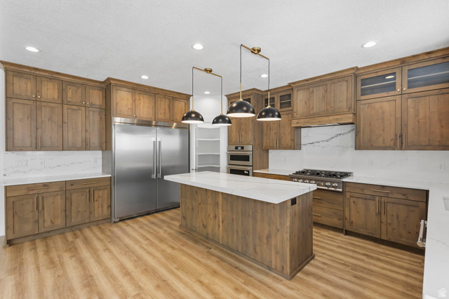 728 East Mountain Road North Ogden, UT 84414 - Photo 9 of 28 Open-concept kitchen featuring a central island with a white countertop, wood-finish flooring, full-height cabinetry with crown molding, stainless steel appliances, and ceiling-mounted pendant lighting