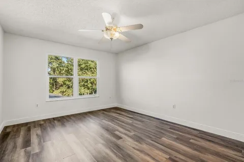 an empty room with wooden floor chandelier fan and windows