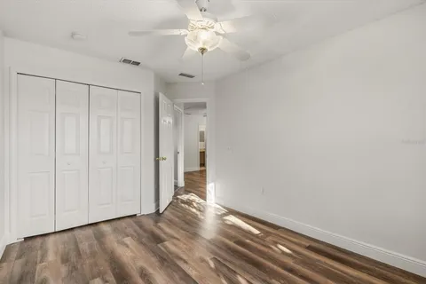 a view of an empty room with chandelier fan and wooden floor