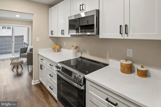 a kitchen with stainless steel appliances a sink a stove and white cabinets with wooden floor