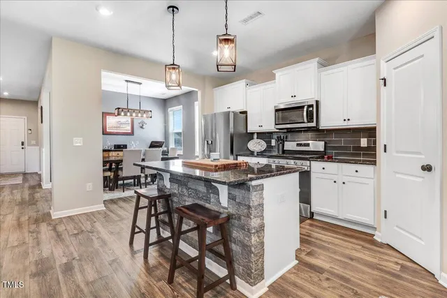 a kitchen with stainless steel appliances granite countertop a stove top oven a refrigerator a sink and a dining table with wooden floor