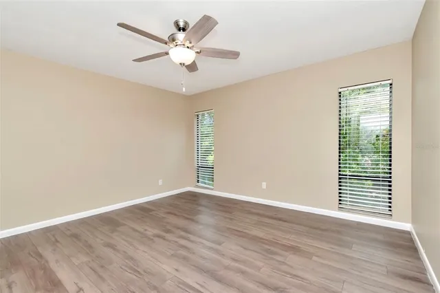 an empty room with wooden floor chandelier fan and windows
