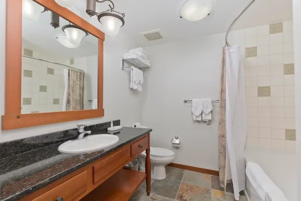 a bathroom with a granite countertop sink a toilet a mirror and shower