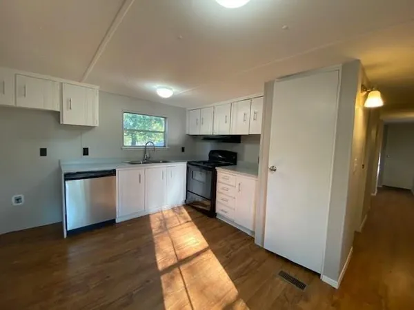 a kitchen with granite countertop a refrigerator oven a sink dishwasher and white cabinets with wooden floor