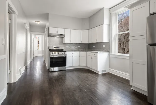 a kitchen with stainless steel appliances granite countertop a refrigerator a stove a sink and white cabinets with wooden floor