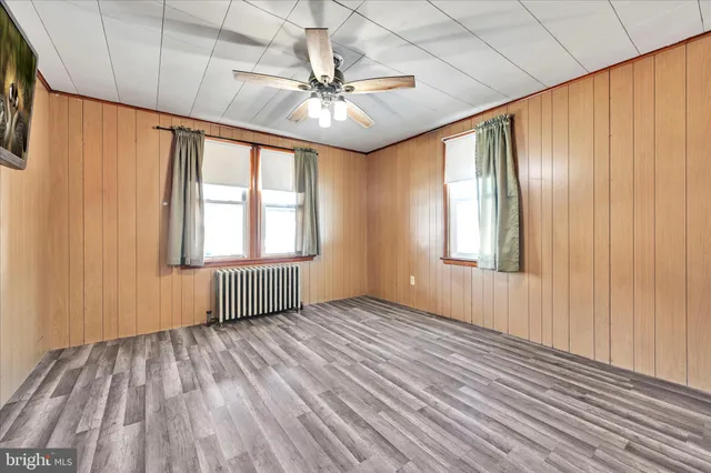 an empty room with wooden floor fan and windows