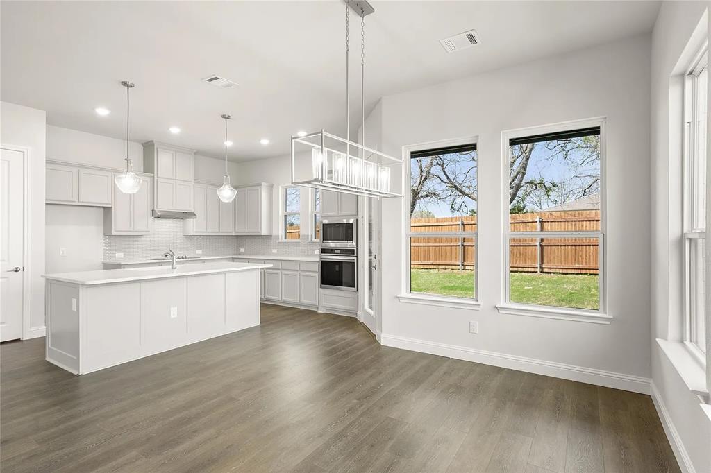 4021 Alpine Street Midlothian, TX 76065 - Photo 7 of 18 Open-concept kitchen and dining area featuring wood-finish flooring, white cabinetry, a large kitchen island with a white countertop, stainless steel appliances, and a modern rectangular chandelier