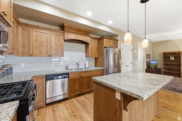 7235 Viansa Court Midvale, UT 84047 - Photo 10 of 43 Kitchen featuring wood finish cabinetry, a kitchen island, stainless steel appliances, light wood-style floors, and light stone counters