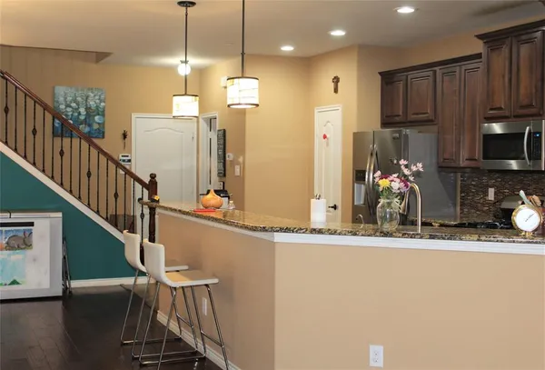 a kitchen with stainless steel appliances kitchen island granite countertop a refrigerator a stove and a sink with wooden floor