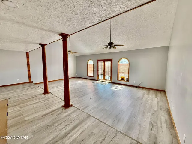 a view of an empty room with wooden floor and fan