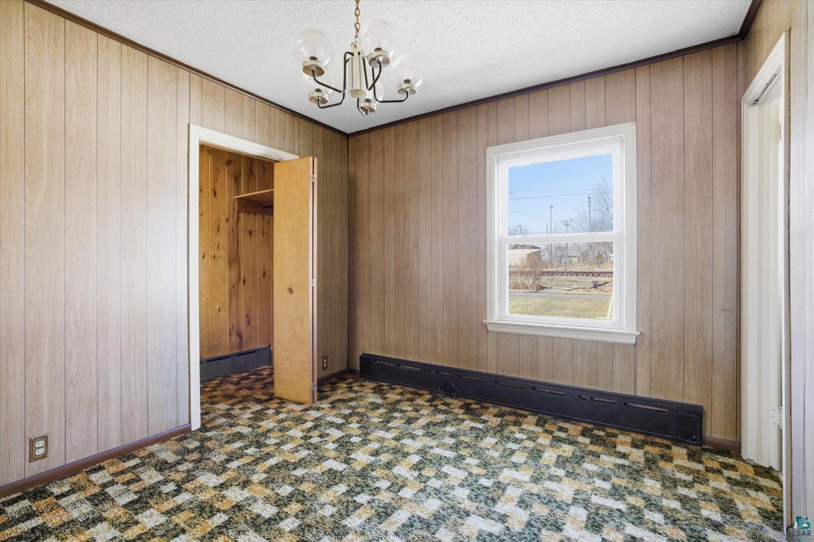 709 Michigan Street Hibbing, MN 55746 - Photo 37 of 47 Unfurnished dining area featuring baseboard heating, a chandelier, wood walls, a textured ceiling, and crown molding