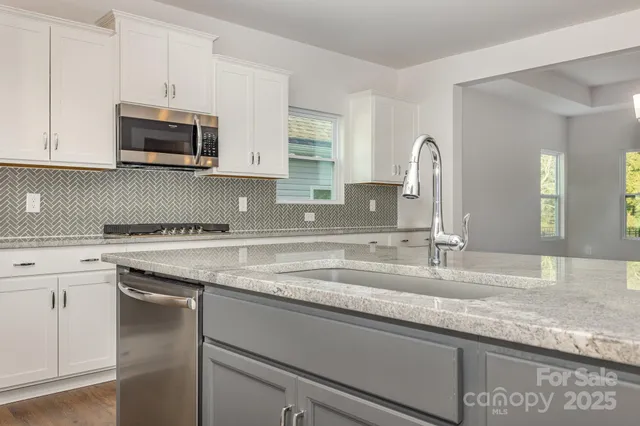 a kitchen with granite countertop a sink stainless steel appliances and white cabinets