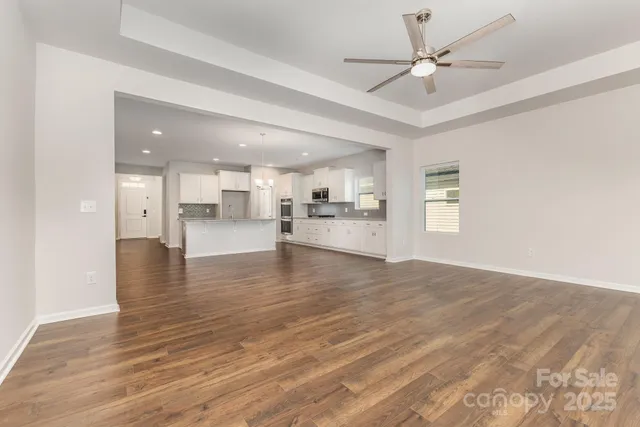 a view of an empty room and kitchen with wooden floor