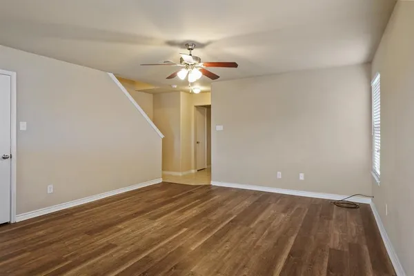 a view of an empty room with wooden floor and a ceiling fan