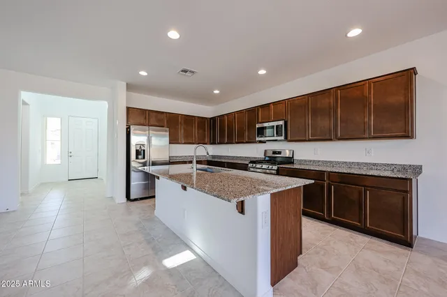 a large kitchen with stainless steel appliances granite countertop a stove top oven a sink and a refrigerator