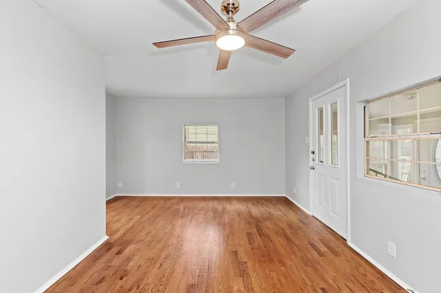 an empty room with wooden floor chandelier fan and windows