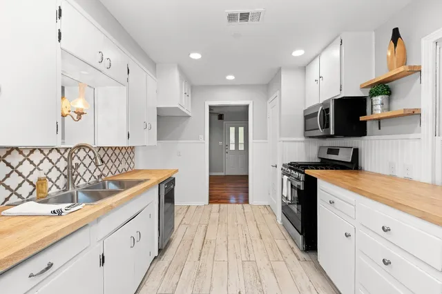 a kitchen with stainless steel appliances granite countertop a refrigerator a stove top oven a sink dishwasher and white cabinets with wooden floor