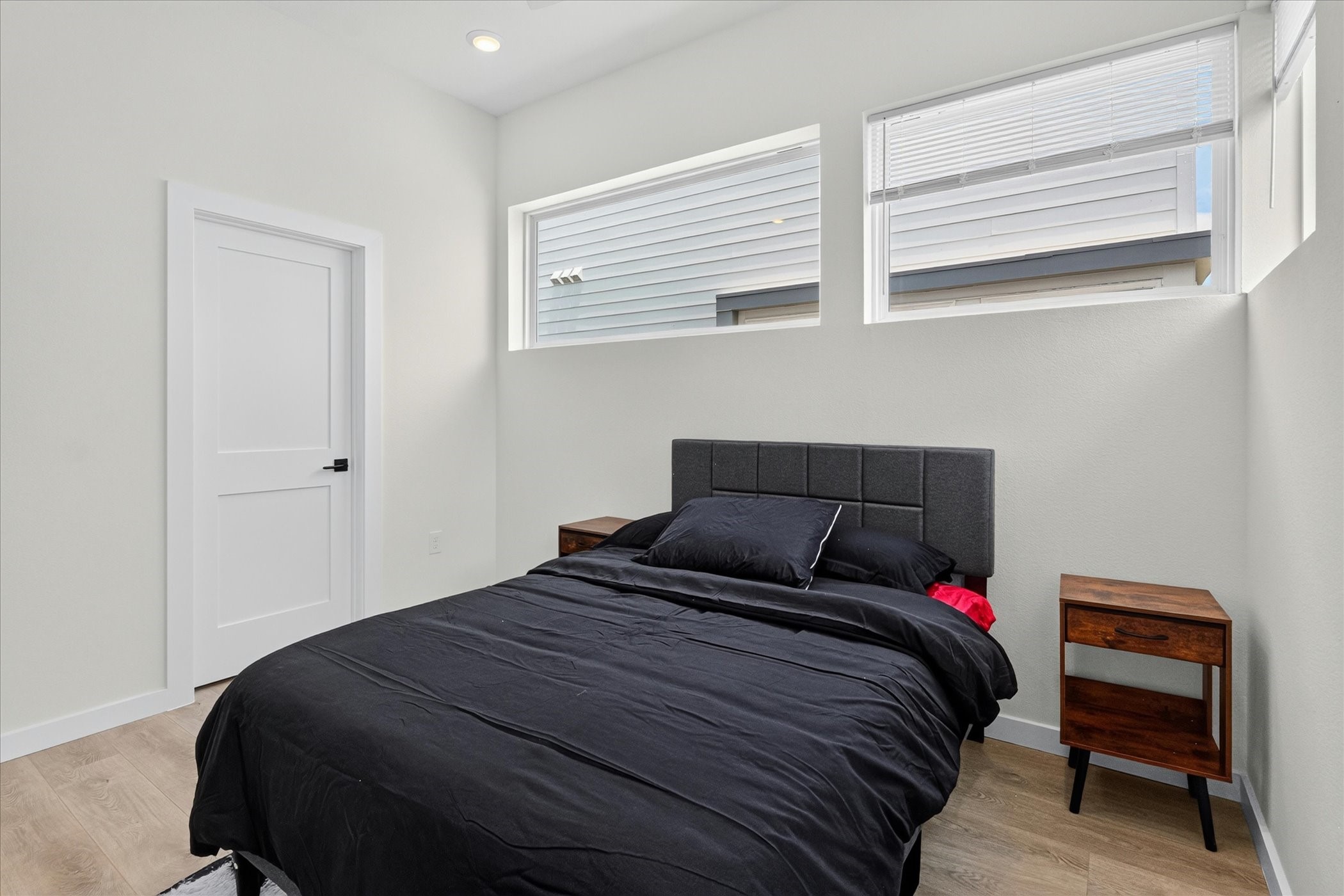 2000 Riverside Farms Road, Unit 8101 Austin, TX 78741 - Photo 29 of 41 This cozy bedroom features natural light from two high windows, a modern black bed, and a wooden nightstand, complemented by light-colored walls and wood flooring.