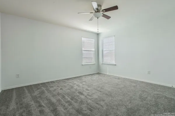 an empty room with chandelier fan and windows