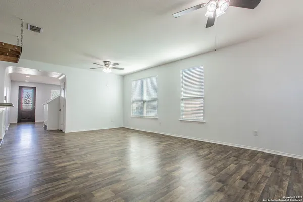 an empty room with wooden floor chandelier and windows