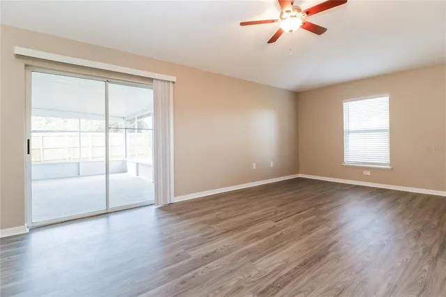 an empty room with wooden floor fan and windows