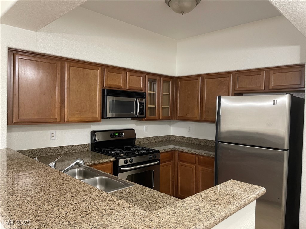 10217 King Henry Avenue, Unit 104 Las Vegas, NV 89144 - Photo 7 of 18 Kitchen with stainless steel appliances, glass insert cabinets, light stone countertops, and brown cabinets