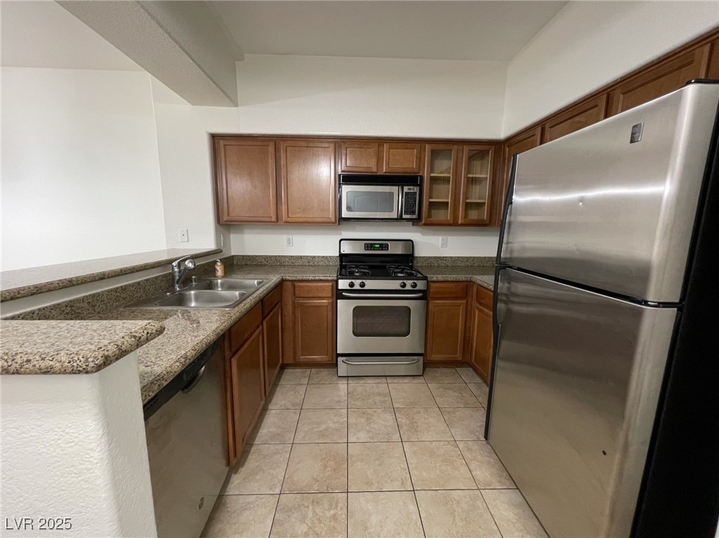 10217 King Henry Avenue, Unit 104 Las Vegas, NV 89144 - Photo 8 of 18 Kitchen with appliances with stainless steel finishes, brown cabinets, light tile patterned floors, and a peninsula