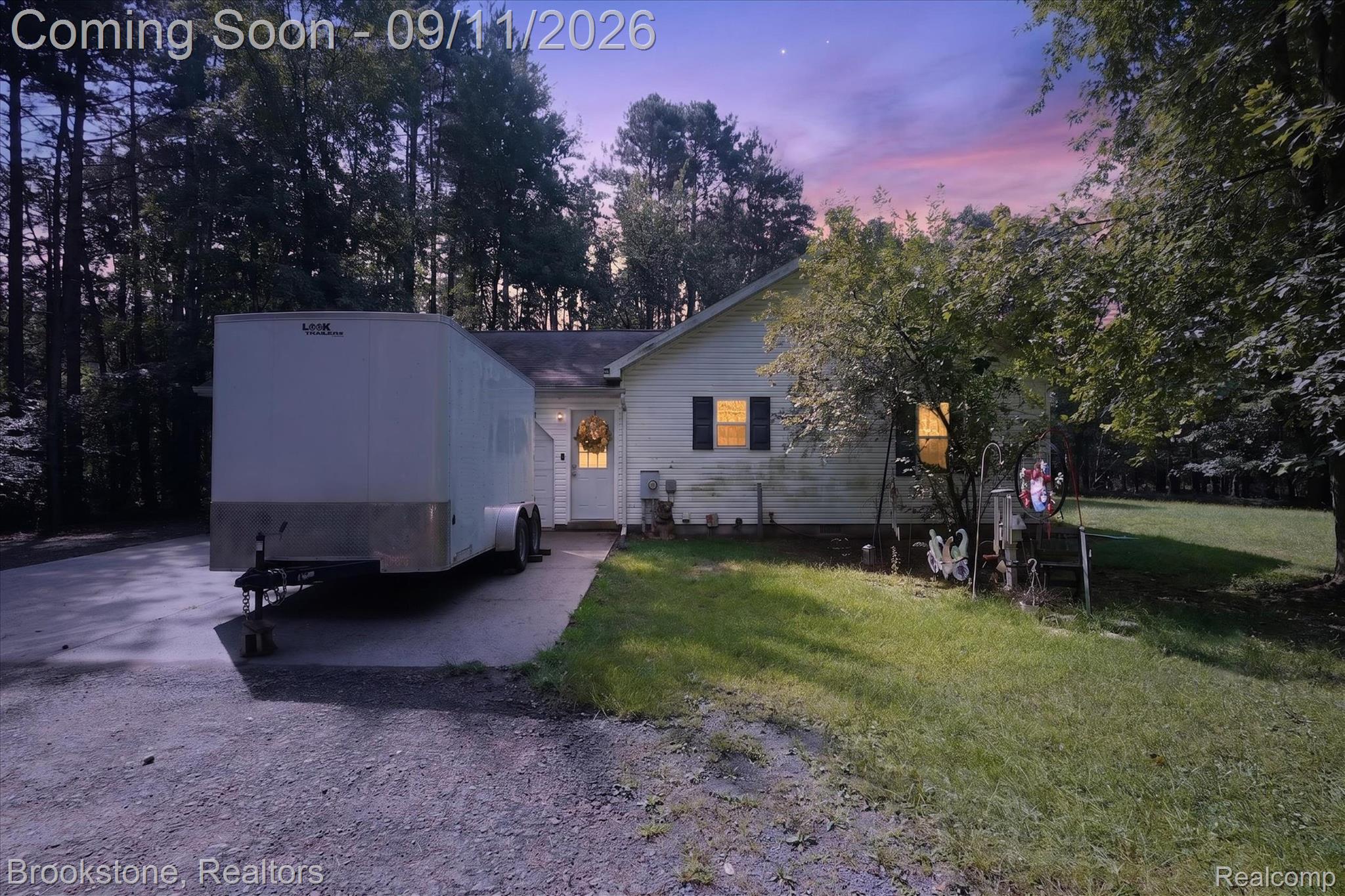 1812 South Steel Road Merrill, MI 48637 - Photo 1 of 39 Twilight exterior showcasing a single-story residence with illuminated windows, positioned on a wooded lot with mature pine and deciduous trees