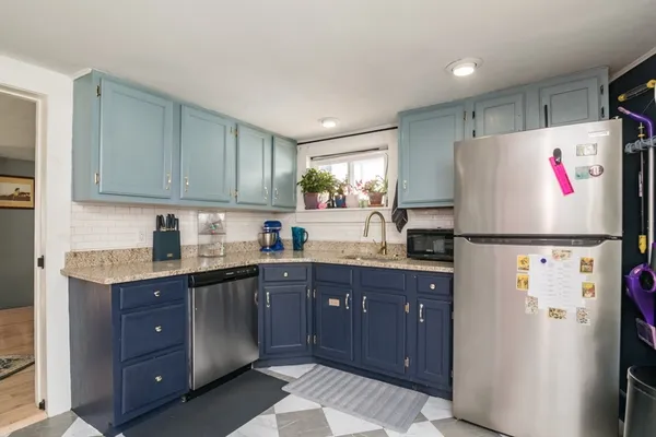 a kitchen with granite countertop a refrigerator a sink and white cabinets
