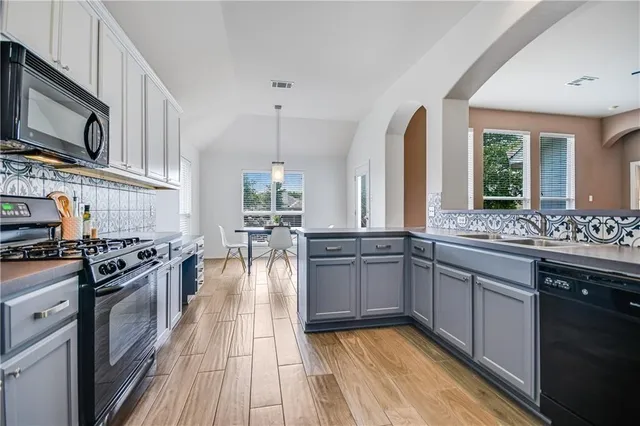 a kitchen with stainless steel appliances granite countertop a stove top oven a sink dishwasher a dining table and chairs with wooden floor