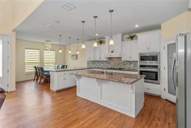 a kitchen with stainless steel appliances kitchen island granite countertop a stove a sink a refrigerator and white cabinets with wooden floor