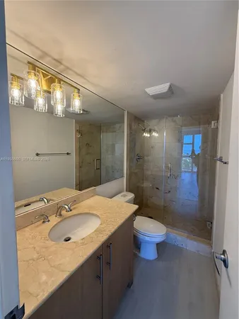 a bathroom with a granite countertop sink a toilet a mirror and shower