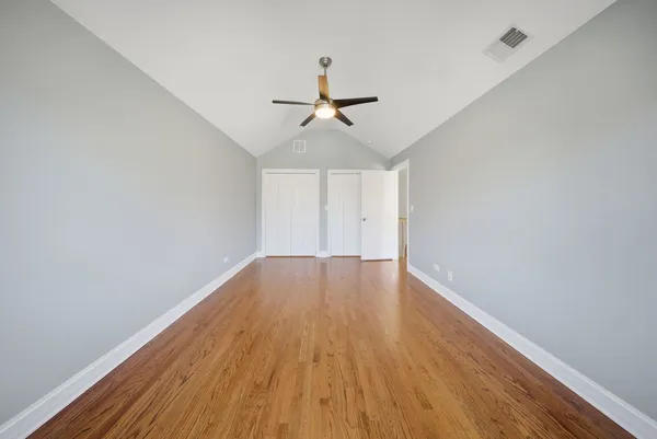 an empty room with wooden floor ceiling fan and windows