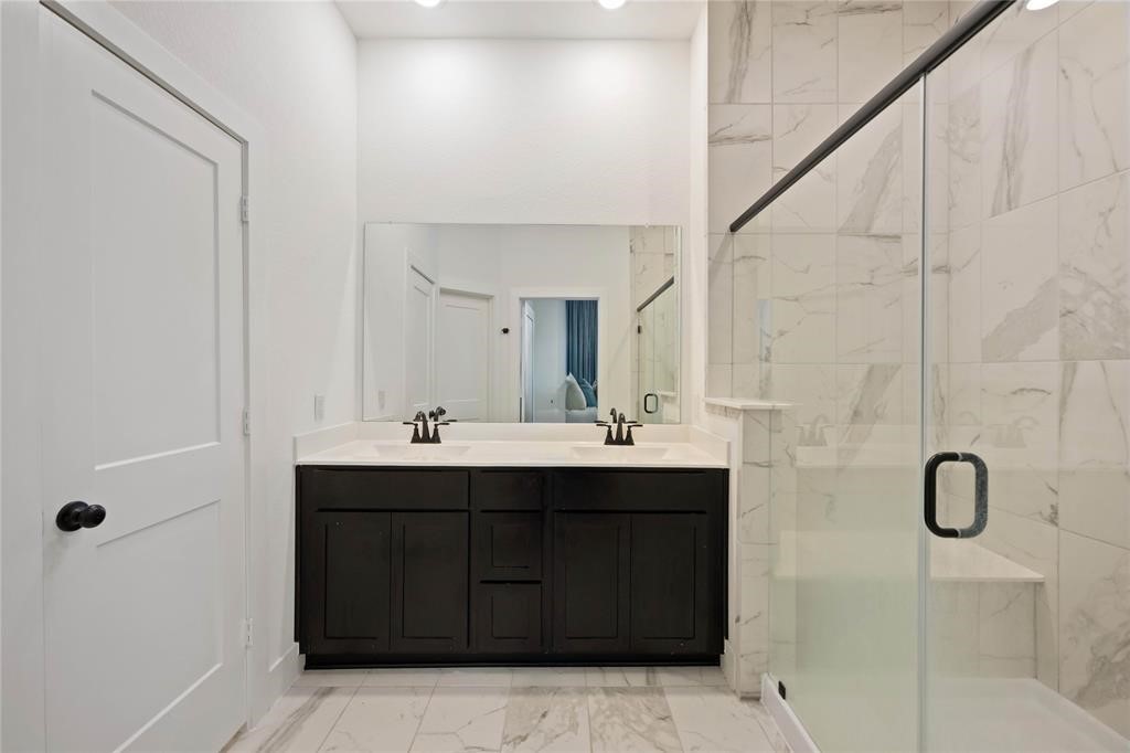 10014 Nectar Path Iowa Colony, TX 77583 - Photo 21 of 26 This bathroom features a modern design with a sleek double vanity, large mirror, and a spacious glass-enclosed shower. The white and gray marble tiles add a touch of elegance.