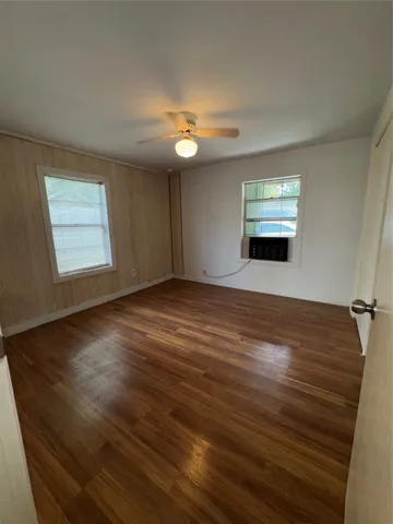 a view of an empty room with wooden floor and a ceiling fan