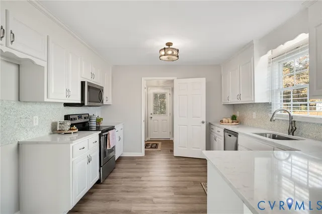 a kitchen with granite countertop a stove top oven a sink dishwasher and white cabinets with wooden floor