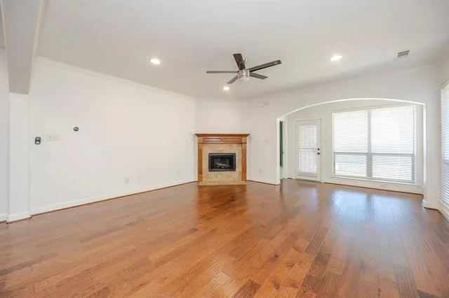 an empty room with wooden floor ceiling fan and windows