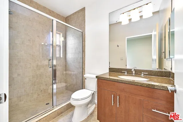 a bathroom with a granite countertop sink a toilet a mirror and shower