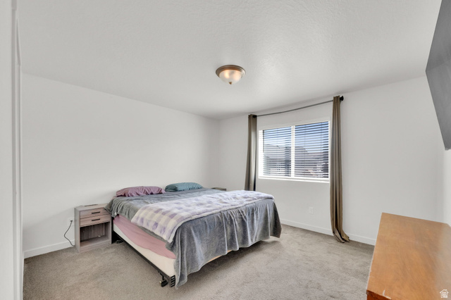 6120 North Sheps Ridge Road Eagle Mountain, UT 84005 - Photo 10 of 43 Bright bedroom featuring a large window with blinds, neutral carpet flooring, and a flush mount ceiling light fixture