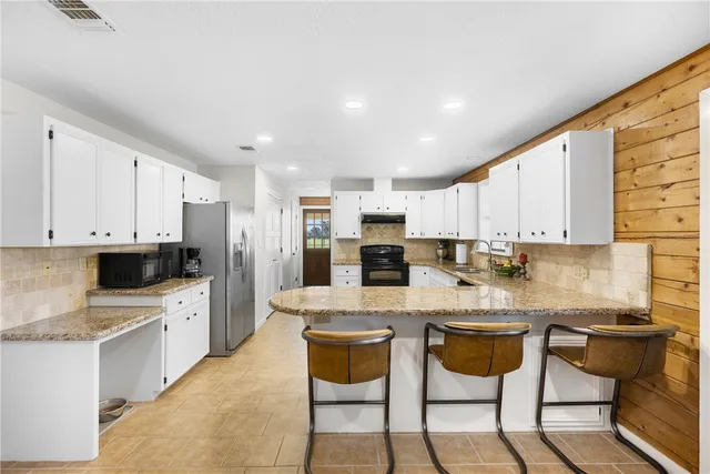 a kitchen with stainless steel appliances kitchen island granite countertop a stove a sink a refrigerator and white cabinets with wooden floor